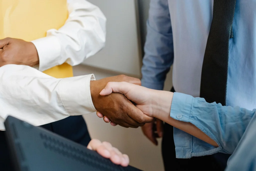 Close-up of two colleagues shaking hands in an office with a third person nearby