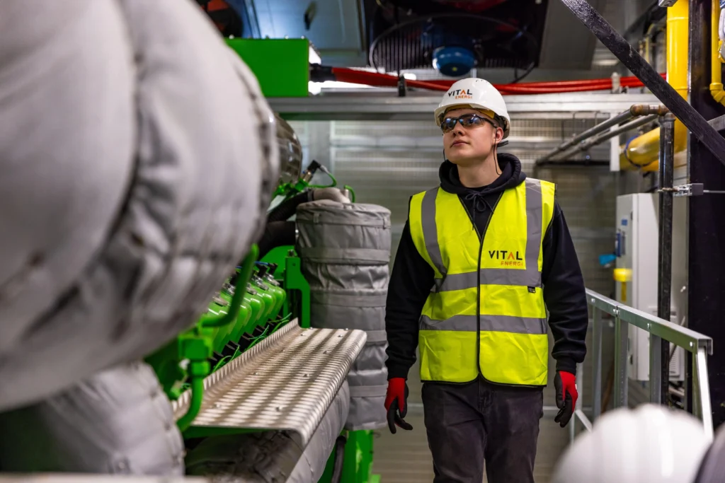 Technician in hi-vis vest and hard hat walking through an industrial energy plant