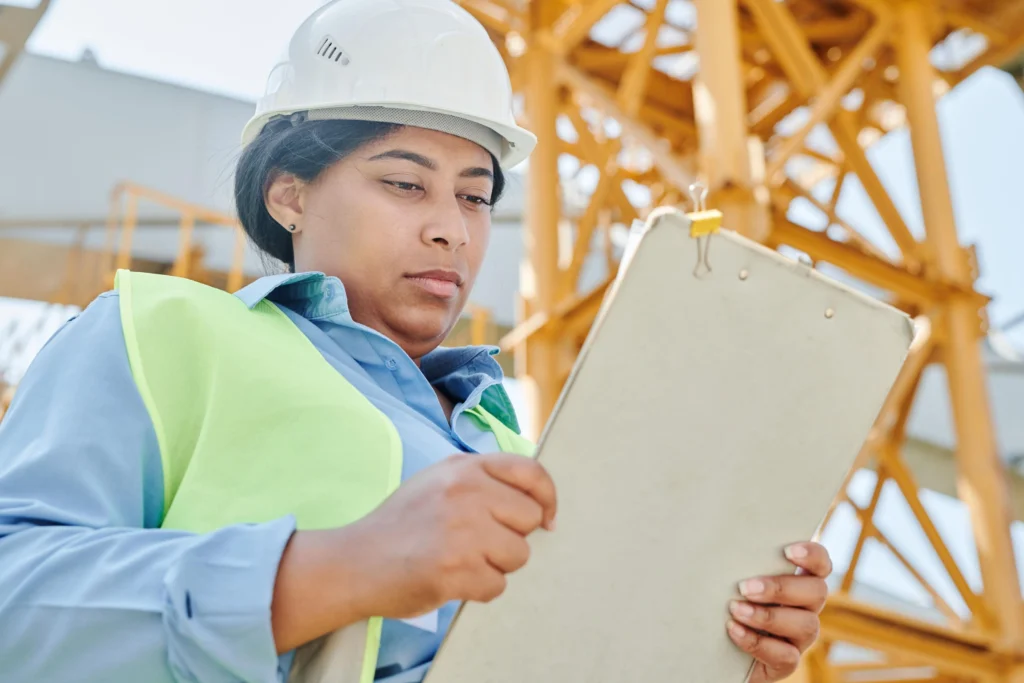 Female construction supervisor in hard hat and hi-vis reviewing a clipboard on site